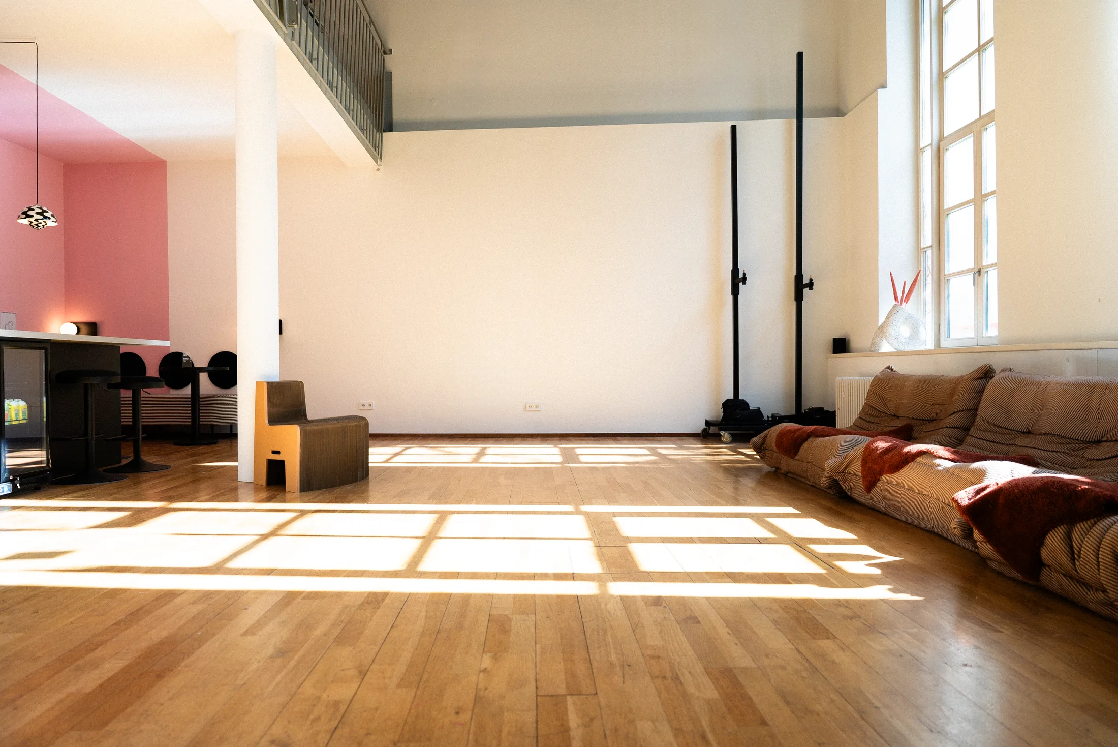 Studiofläche des BAAD Studio mit Fensterlicht auf dem Parkett, rosa Wand und Sitzlandschaft